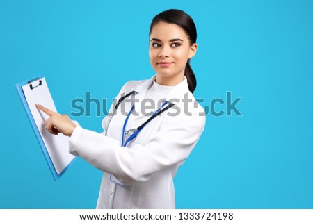 Charming young woman doctor with stethoscope and clipboard over blue background.