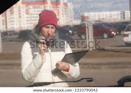 Young woman car insurance agent taking a picture of wrecked car to calculate the damage on a claim form
