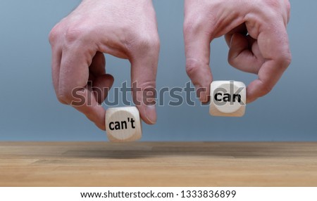 Hands are holding two cubes with the words "can" and "can't". One hand rises the cube with the word "can".