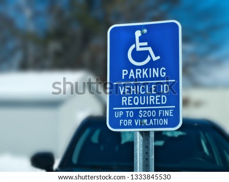 Handicapped parking sign with car, building and tree in snow covered parking lot in winter. Bokeh background.
