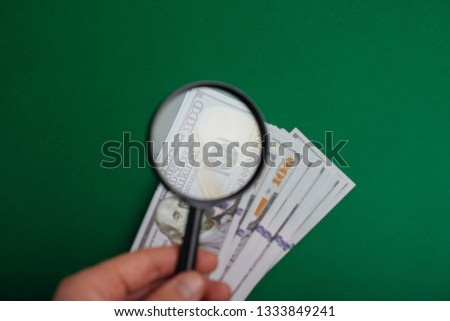 Expert with magnifying glass checks suspicious money. search watermarks on paper of the fake bills.