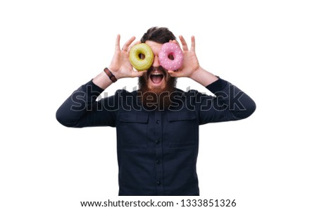 Funny picture of man holding two colorful donuts around his eyes. He is looking on camera and smiling. Guy has some fun.