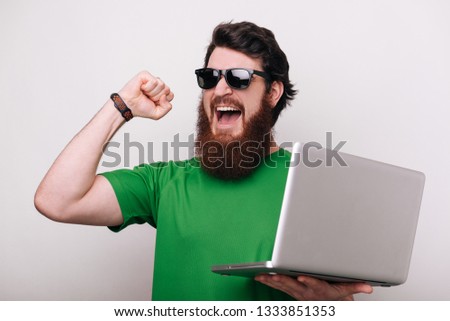 Bearded mna using computer laptop very happy and excited, winner expression celebrating victory screaming with big smile and raised hands