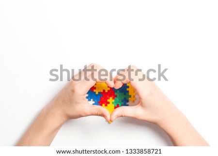 Kid hands in the shape of heart and colorful heart made of plastic construction puzzle pieces on white background. World autism awareness day concept