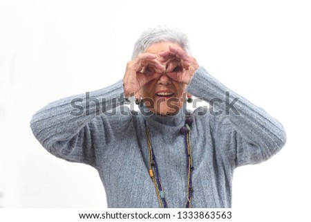 senior woman looking through fingers as if wearing glasses on white background