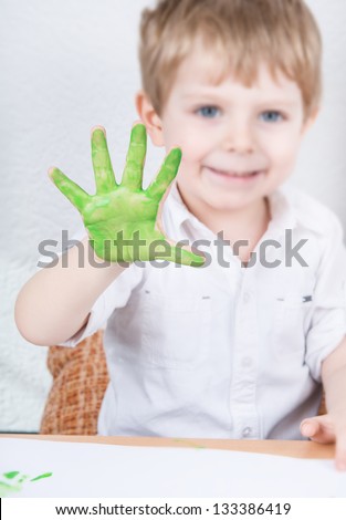 Cute little boy of three years having fun painting at home. Selective focus on painted hand