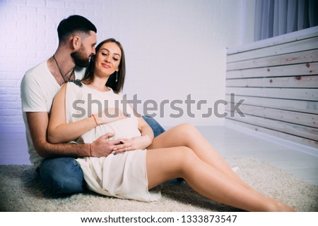 Young pregnant woman with husband sitting on floor hugging stroking belly