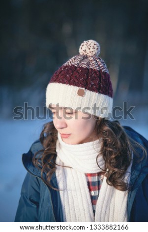 the beautiful young girl in a warm cap from wool of the alpaca in the winter forest