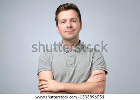 A portrait of young handsome smiling man in t-shirt standing with crossed hands.