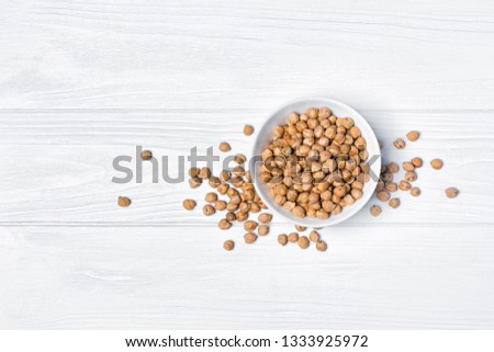Raw chickpeas in bowl as ingredient for vegetarian dish on white wooden background with copy space