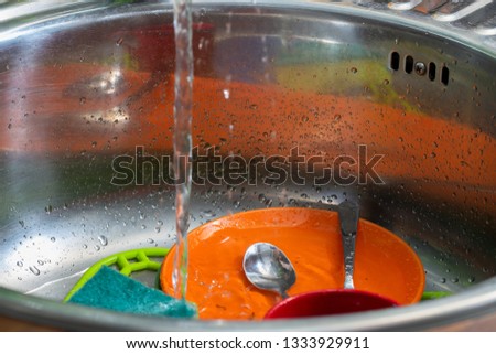 Ware in a metal sink under a stream of water.