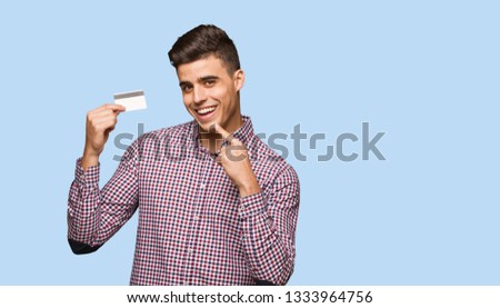 Young man holding credit card smiles, pointing mouth