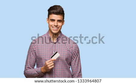Young man holding credit card cheerful with a big smile