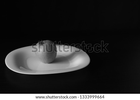 Black and white photo with a ripe Apple on a white porcelain plate, made on a black background. Stylish image for office, catalogs and covers. Monochrome image of an Apple.