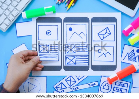 Working desk with hands sorting wireframe screens of mobile responsive website. Developing wireframe sketch layout design mockup on smartphone,tablet screen.