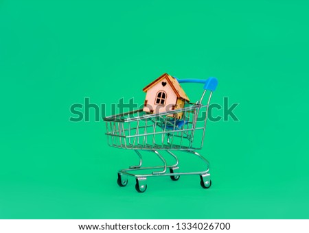 Shopping cart with miniature house on turquoise background
