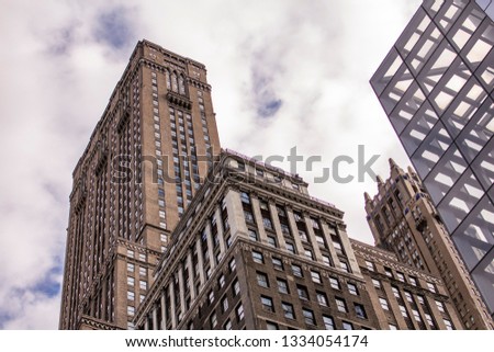 An upward photo of buildings in Manhattan with clouds in the sky above