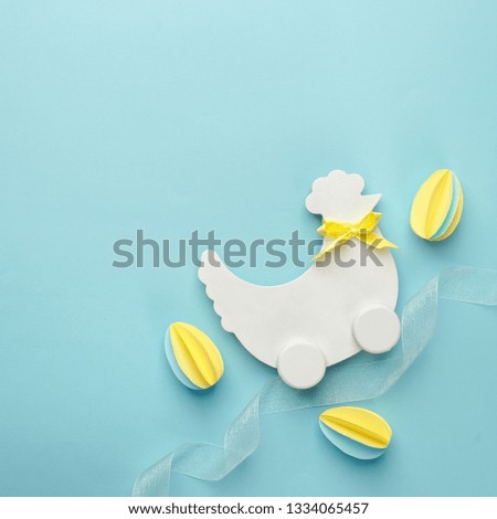 Easter holiday creative background with papercraft eggs, white wooden chicken hun on pastel blue table, trendy paper craft holiday background, top view, copy space