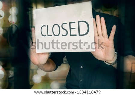 Failed business going down or opening times concept. Man putting closed sign in window in shop. Late at night in city.