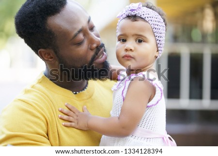 African father holds his little daughter in his arms, hugs and kisses.