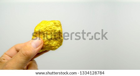 Hand holding a piece of gold chunk in front of white background Royalty-Free Stock Photo #1334128784