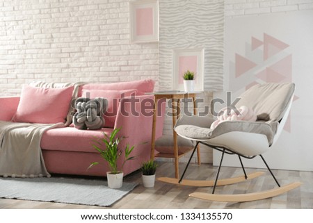Stylish living room interior with sofa and rocking armchair near brick wall