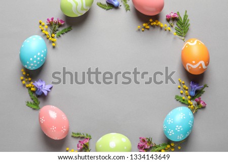 Flat lay composition of painted Easter eggs and flowers on color background, space for text