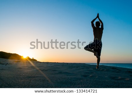 Fit young man practices sun salutation yoga on the beach at sunset Royalty-Free Stock Photo #133414721