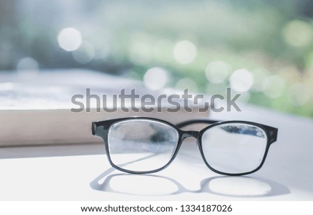 The glasses are placed on a laptop on a wooden table in the library and there are many books as blur background, beautiful bokeh, soft light, concepts and knowledge about research in the library.