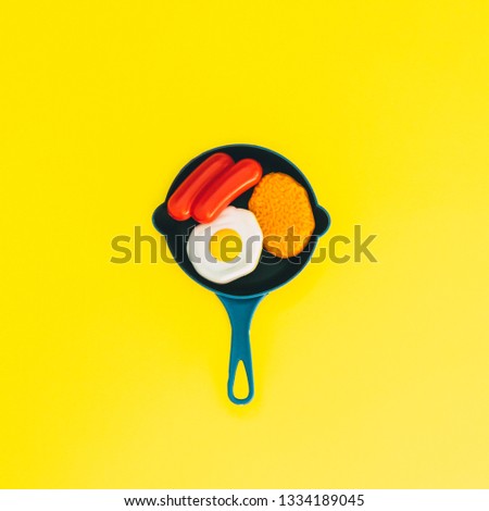 Fried eggs, omelettes and sausages in pan  on a yellow background. The concept of minimalism. 