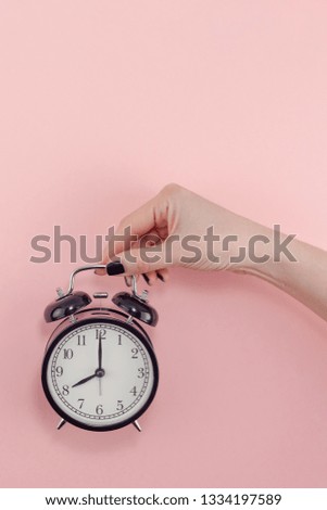 Creative flat lay morning time emotions concept top view of woman hand holding black vintage alarm clock pastel millennial pink color paper background with copy space minimal style template for text