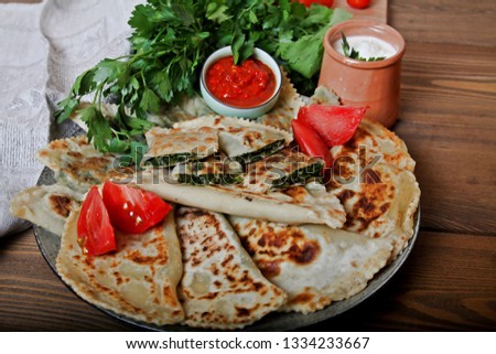 Traditional food flat bread qutab with green stuff herbs tomatoes sour cream, red wine and adjika