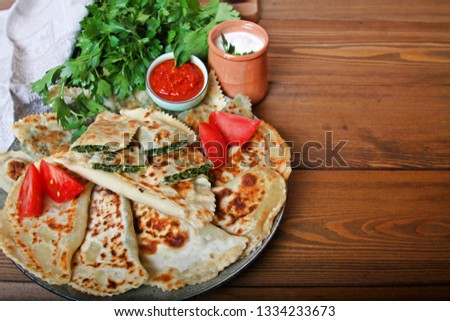 Traditional food flat bread qutab with green stuff herbs tomatoes sour cream, red wine and adjika