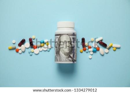 Money and pills of different colors on blue background. Rising cost of health care.
