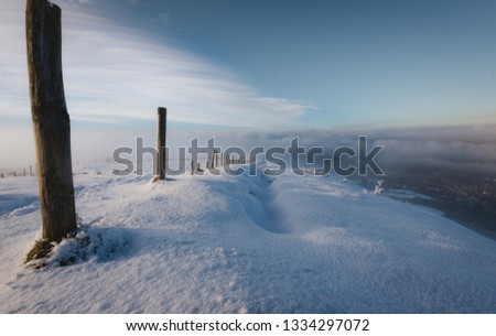 A line of Wooden Posts guide the viewer down a snowy hill into the valley below covered in fog and low cloud, Peak District