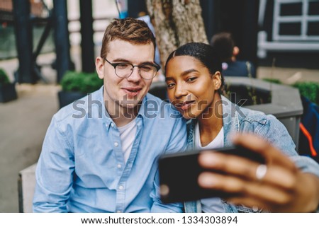 Happy multicultural millennial young friends making selfie at front camera of modern smartphone.Diverse couple photographing themselves on mobile phone for social networks sitting in urban setting