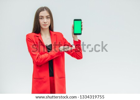 Young pretty pretty girl wearing a red jacket. Stays on a gray background. During this time, holds a black phone. Green screen.