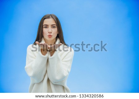 Young beautiful brunette woman on an isolated background. Showing an air kiss with his hands and mouth. Smiling confidently and happily.