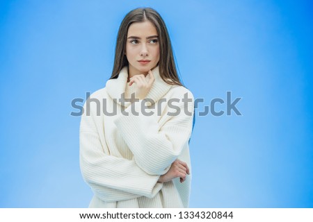 Picture of happy young lady standing on a blue background. Look into the camera. During this time she is dressed in a white warm sweater.