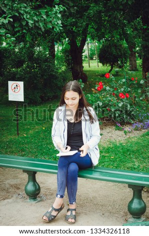 A young girl sits on a bench in the garden and draws.