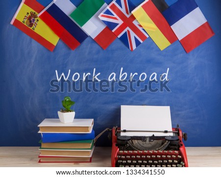 work abroad concept - red typewriter, flags of Spain, France, Great Britain, books and other countries and blackboard with text "Work abroad" Royalty-Free Stock Photo #1334341550