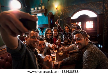 group of millennial people takes a selfie in a pub drinking beer and eating snacks
