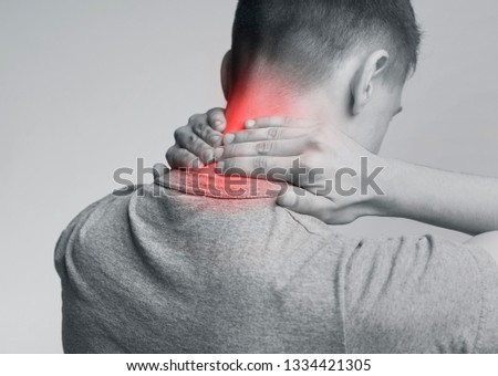 Young man with neck pain, massaging red injured zone, back view. Monochrome photo with red inflamed zone