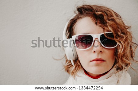 Beautiful young woman in a sunglasses and headphones listening to music standing at the wall. Casual style concept.