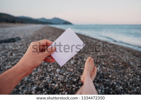 Empty paper note in hand on amazing landscape background. Travel and Vacation concept. White piece of paper with no text