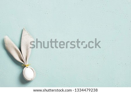 Background with Easter egg  decorated with bunny ears of linen napkin on the blue textured table, top view, copy space