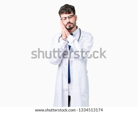 Young doctor man wearing hospital coat over isolated background sleeping tired dreaming and posing with hands together while smiling with closed eyes.