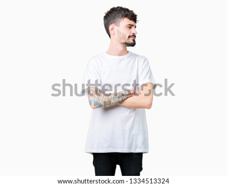 Young handsome man wearing white t-shirt over isolated background smiling looking to the side with arms crossed convinced and confident