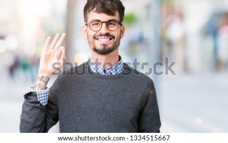 Young handsome smart man wearing glasses over isolated background smiling positive doing ok sign with hand and fingers. Successful expression.