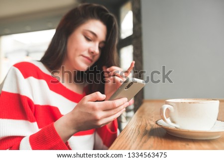 Close up portrait of a young girl uses a smartphone in a cafe, looking at the screen. Focus on the smartphone. Girl holds phone in the hands close up.